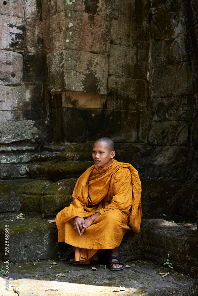 Monk in orange clothes sitting at stone building. Monk in orange clothes sitting at stone building.