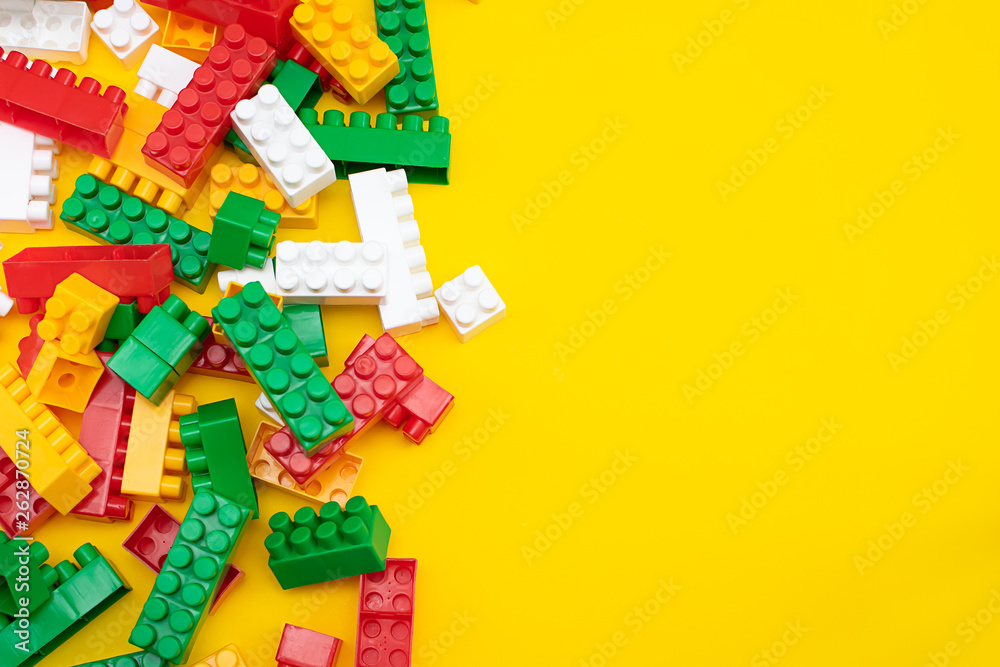 Colorful plastic construction blocks frame on yellow, copy space for your text. Educational children toys on bright yellow background top view.