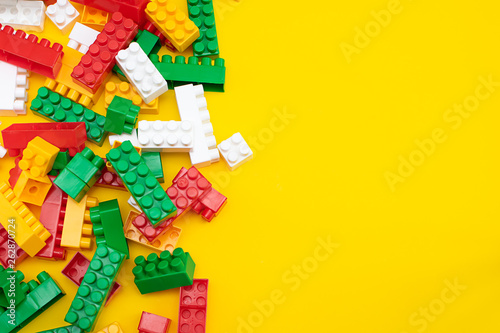 Colorful plastic construction blocks frame on yellow, copy space for your text. Educational children toys on bright yellow background top view.