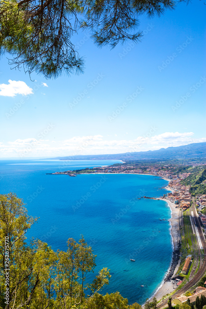 Blue Ionian sea near Taormina luxury resorts coastline, bright sunny summer day. Beautiful tree frame. Sicily island, Italy. 