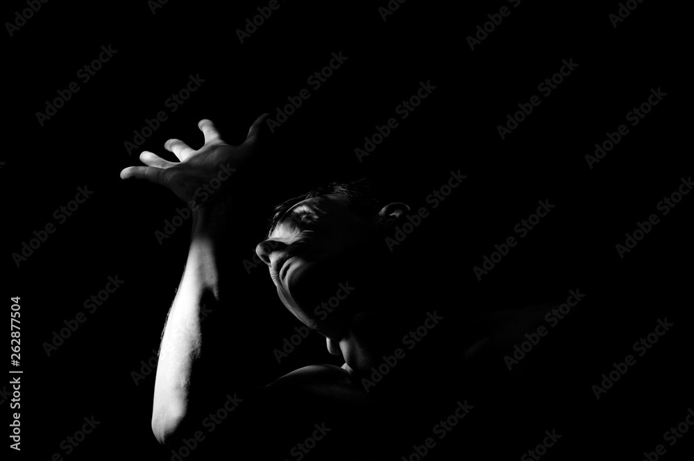 Dramatic black and white photo, a man covers his face with his hand from the light.