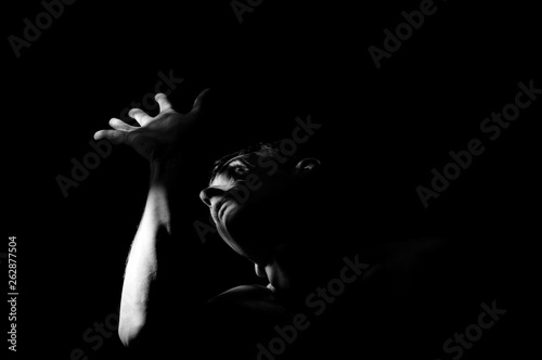 Dramatic black and white photo, a man covers his face with his hand from the light. © Serhii  Holdin