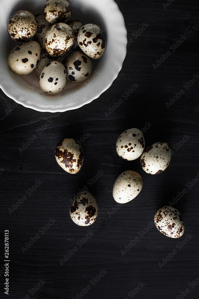 Quail eggs. Flat lay composition with small quail eggs in the bowl on the black wooden background. Quail eggs. Flat lay composition with small quail eggs in the bowl on the black wooden background.