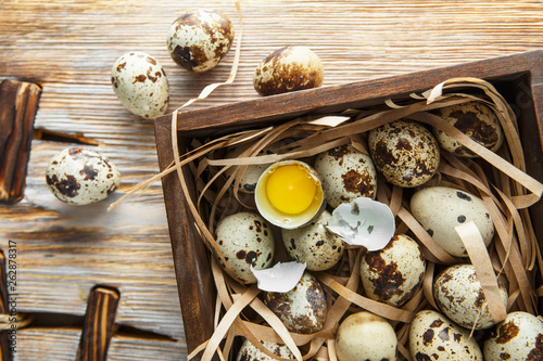 Quail eggs. Flat lay composition with small quail eggs in the wooden box on the natural wooden background. Two broken eggs with a bright yolk.