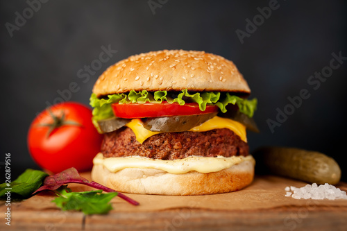 Homemade hamburger with lettuce, tomato, cheese and cucumber on a cutting board