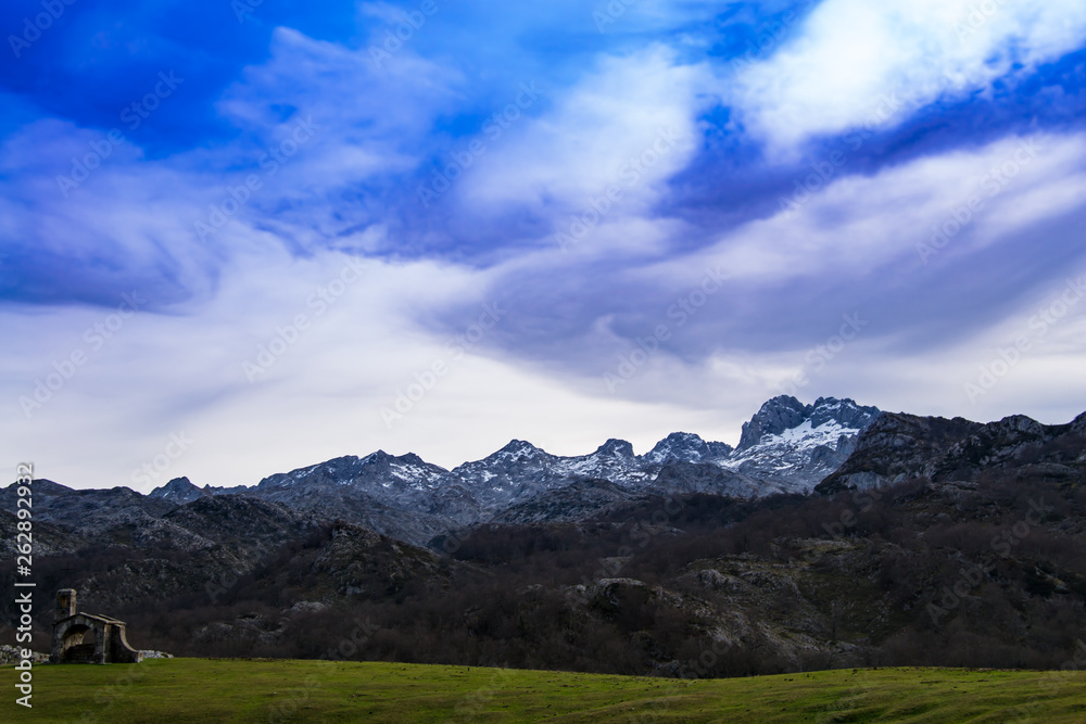 Vieja ermita sobre el campo con las montañas nevadas en el fondo en Asturias, España.