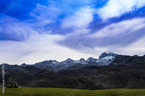 Vieja ermita sobre el campo con las montañas nevadas en el fondo en Asturias, España.