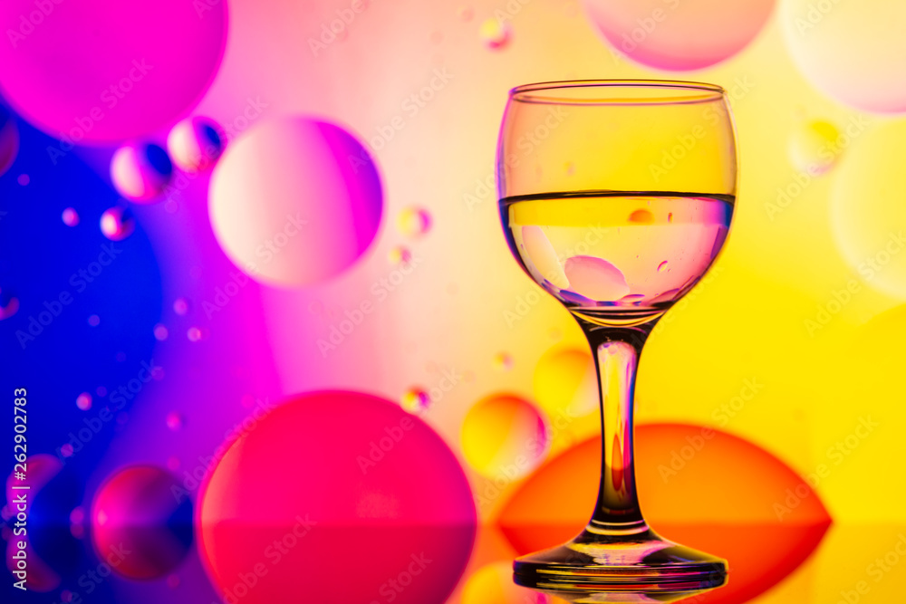 transparent glasses with water and oily drops on colorful background transparent glasses with water and oily drops on colorful background