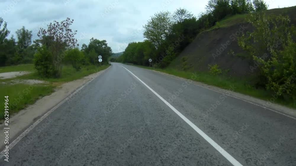 Video background shot in motion from car backwards - 60 fps. An asphalt road outside the city. Green trees along the road. Cloudy, rainy weather. Video background shot in motion from car backwards - 60 fps. An asphalt road outside the city. Green trees along the road. Cloudy, rainy weather.
