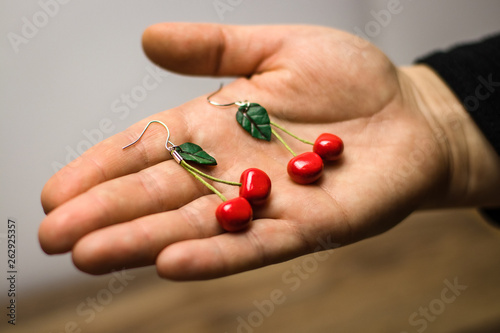 Hand made custom cherry polymer clay earrings on grey fabric background. On hand