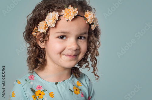Close up portrait of sweet little girl in flower headband on blue background