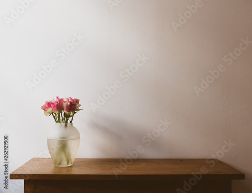 Pink and cream roses on wooden oak side table against neutral wall with moody lighting - warm matte filter effect and selective focus