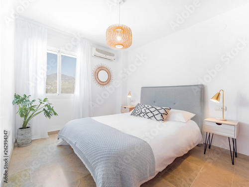Comfortable hotel bedroom with felt headboard with natural fabric cushion, rattan lamp, wood nightstand and a big wooed wardrove.Holiday destination apartment with scandinavian style. photo