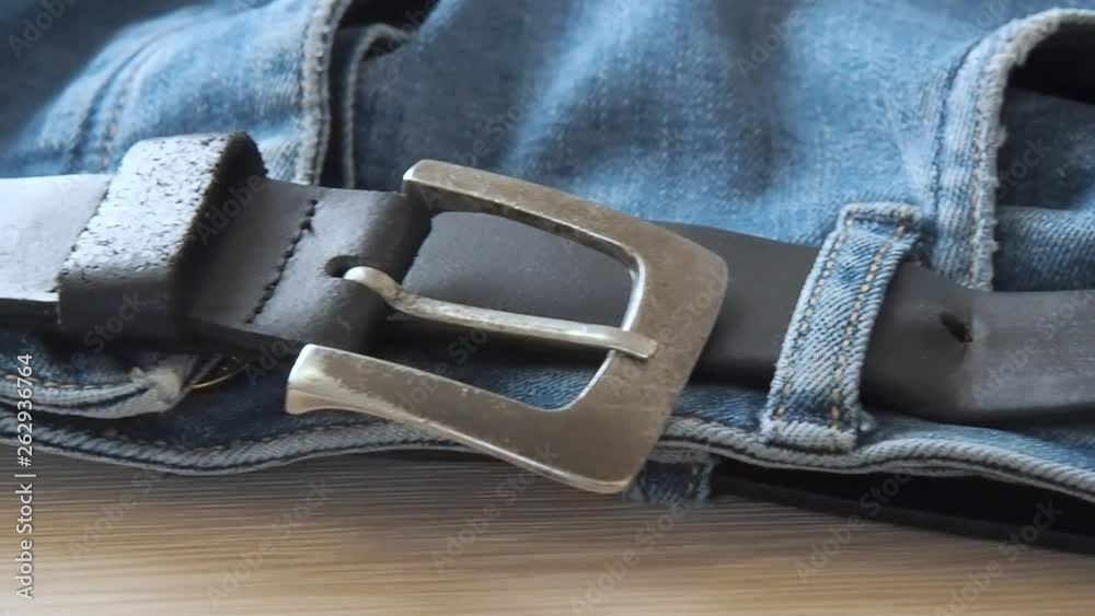 Blue denim jeans laying on the table. Macro dolly shot. Selective soft focus. Camera moving along leather belt. Clothing for everyday wearing. Blue trousers, close view Blue denim jeans laying on the table. Macro dolly shot. Selective soft focus. Camera moving along leather belt. Clothing for everyday wearing. Blue trousers, close view