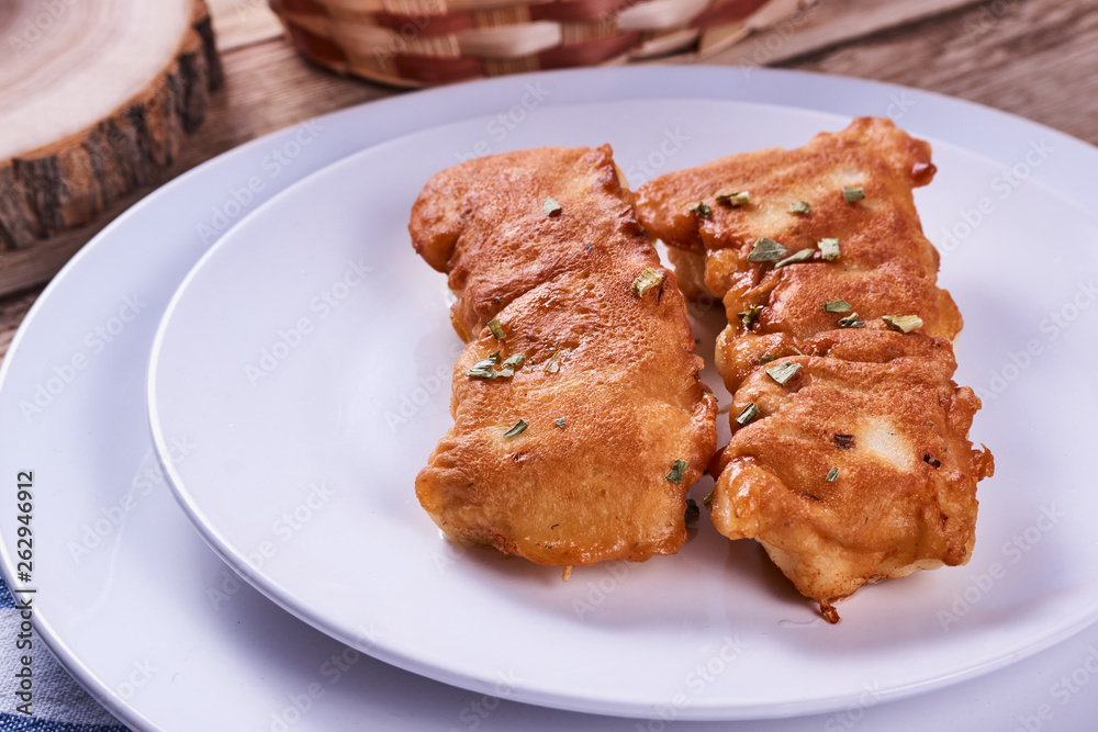 Deep-fried battered cod fillets, in a white plate next to onions and bread on a wooden background. Close-up Deep-fried battered cod fillets, in a white plate next to onions and bread on a wooden background. Close-up
