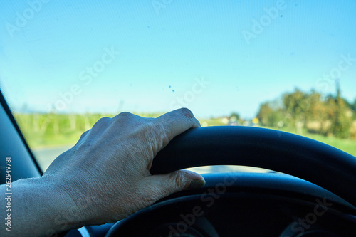 Female hands on the steering wheel of a car while driving and road background