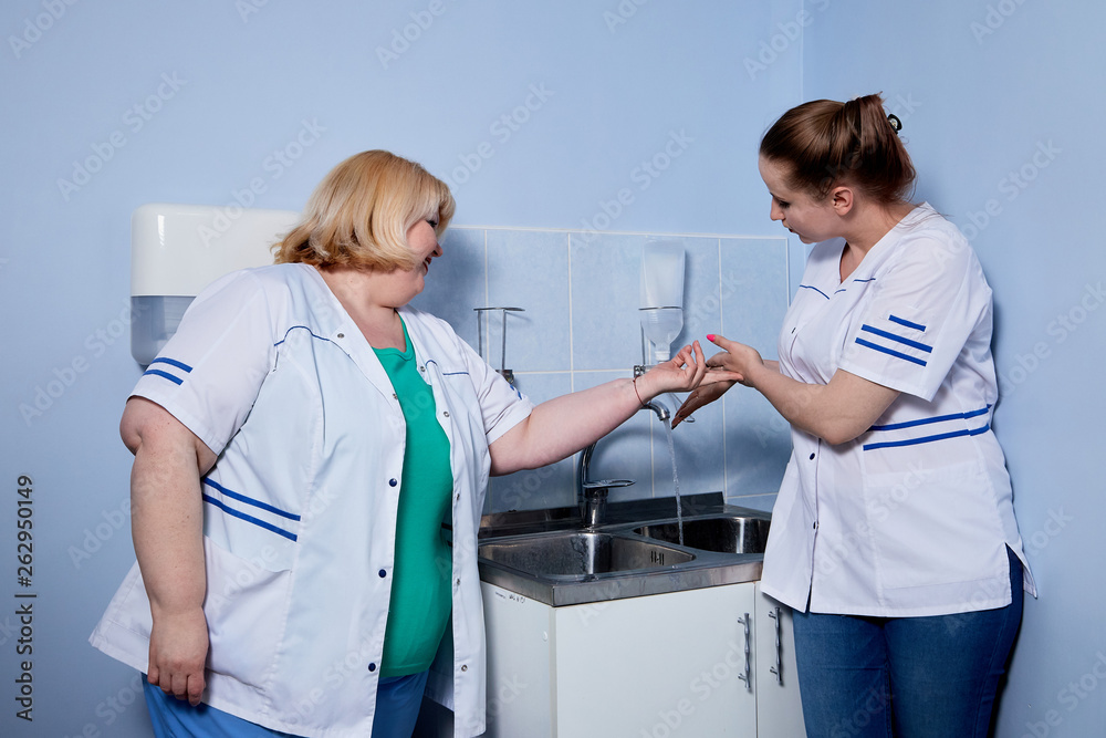Obraz premium Experienced doctor fat woman teaching aspiring young doctor how to wash handsand before meeting with the patient