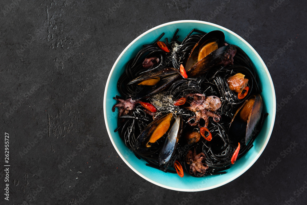 Top view of mediterranean black pasta with seafood. Spaghetti Nera with cuttlefish ink, mussels, shrimp and red chili pepper on blue plate. on dark background. Top view of mediterranean black pasta with seafood. Spaghetti Nera with cuttlefish ink, mussels, shrimp and red chili pepper on blue plate. on dark background.