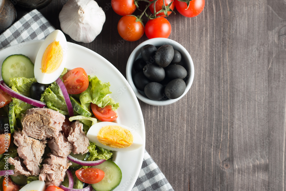 Fresh Caesar tuna salad with delicious tuna fish, ruccola, spinach, cabbage, arugula, egg, parmesan and cherry tomato on wooden background. Oil, salt and pepper. Healthy and diet food concept. Fresh Caesar tuna salad with delicious tuna fish, ruccola, spinach, cabbage, arugula, egg, parmesan and cherry tomato on wooden background. Oil, salt and pepper. Healthy and diet food concept.