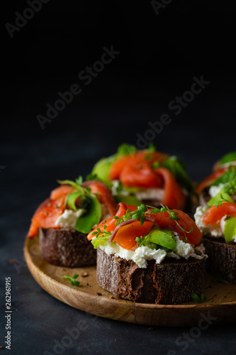 Homemade toast sandwich with rye bread, salmon, avocado, cottage cheese and microgreen sprouts on dark background. Healthy food - breakfast