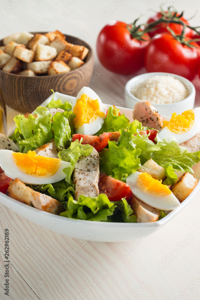 Fresh Caesar salad with delicious chicken breast, ruccola, spinach, cabbage, arugula, egg, parmesan and cherry tomato on wooden background. Oil, salt and pepper. Healthy and diet food concept. Fresh Caesar salad with delicious chicken breast, ruccola, spinach, cabbage, arugula, egg, parmesan and cherry tomato on wooden background. Oil, salt and pepper. Healthy and diet food concept.