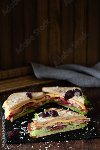A club sandwich on a dark table with ham, cheese, bacon and lettuce close-up.