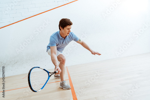 Emotional sportsman in blue polo shirt playing squash in four-walled court photo