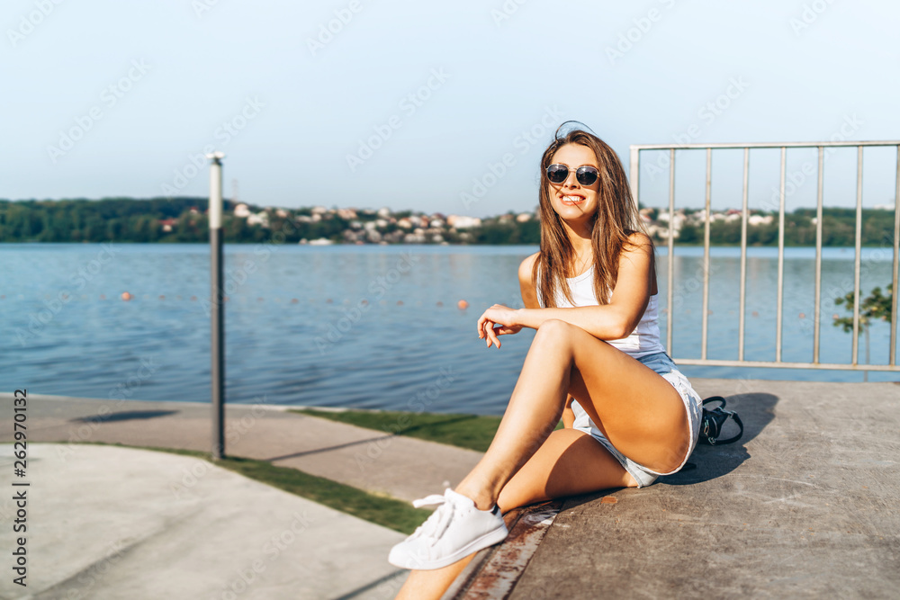 Pretty young brunette girl with long hair relaxing outdoor in the park near lake.