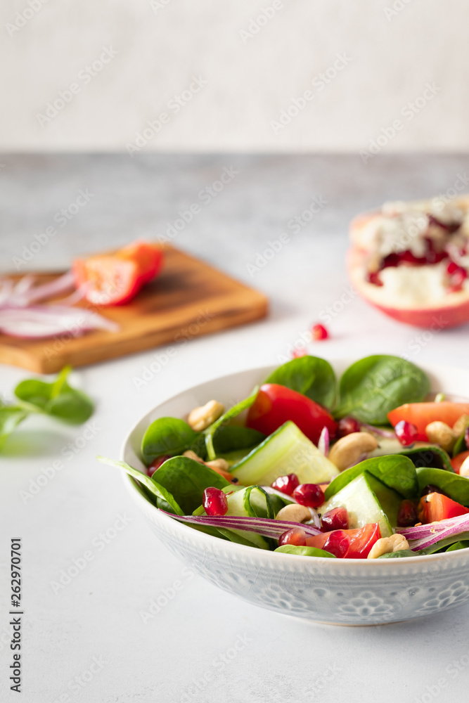Healthy classical vegetable fresh salad of spinach, tomato, cucumber, onion, cashew nuts, pomegranate and sesame with olive oil dressing on white plate and white background. Diet menu. Healthy classical vegetable fresh salad of spinach, tomato, cucumber, onion, cashew nuts, pomegranate and sesame with olive oil dressing on white plate and white background. Diet menu.