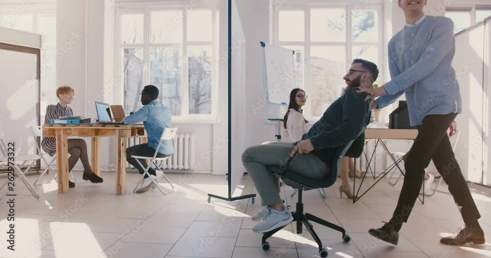 Dolly side view shot of crazy fun businessman riding office chair along big busy workplace hall, celebrating achievement Dolly side view shot of crazy fun businessman riding office chair along big busy workplace hall, celebrating achievement