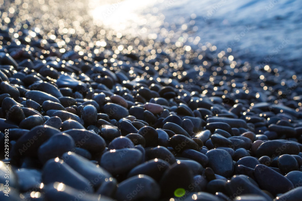 Obraz premium Wet pebbles shine on seashore in the morning at sunset