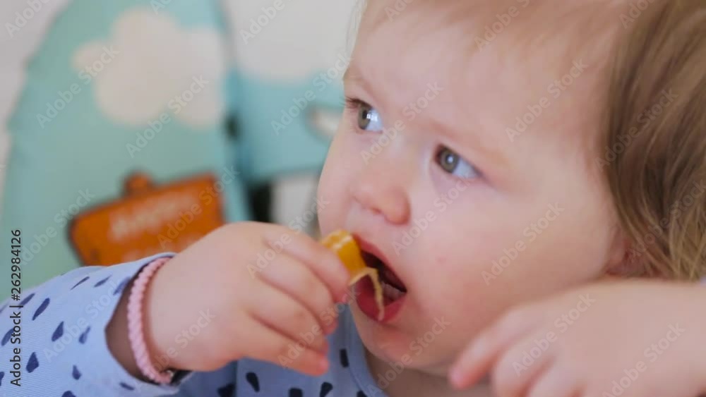 A little girl sitting on a high chair and eating different vegetables and fruits A little girl sitting on a high chair and eating different vegetables and fruits