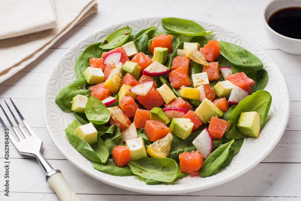 Poke Hawaiian salad with salmon, avocado spinach and vegetables in a plate on a white table.