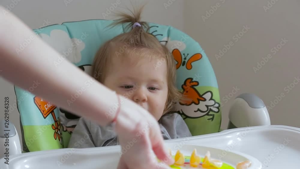 A little girl sitting on a high chair and eating different vegetables and fruits A little girl sitting on a high chair and eating different vegetables and fruits