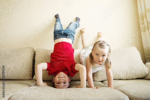 Obraz na plátne Brother and sister playing on the couch: the boy stands upside down