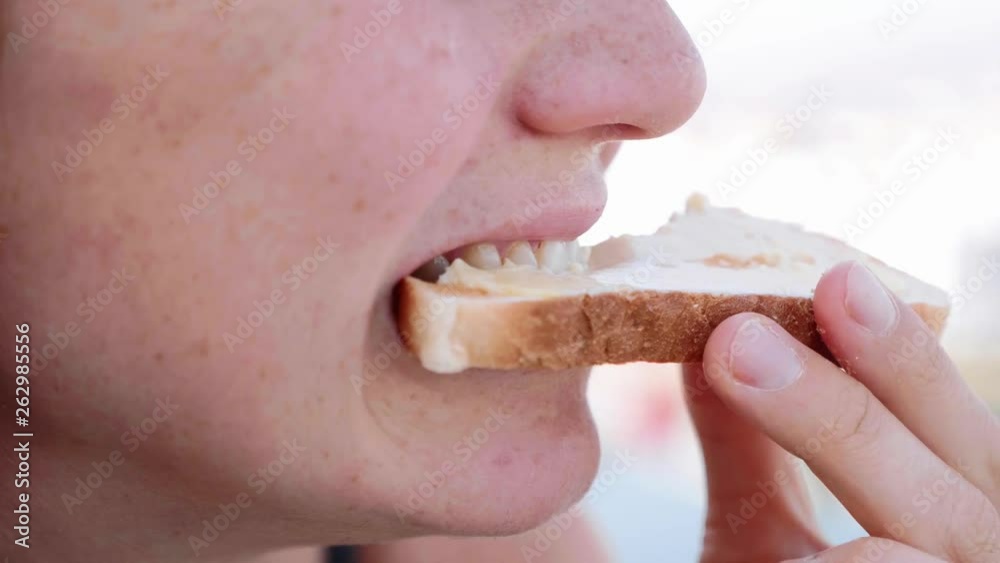Close-up of woman's mouth is bites off toast and chews it in slow motion, side view.