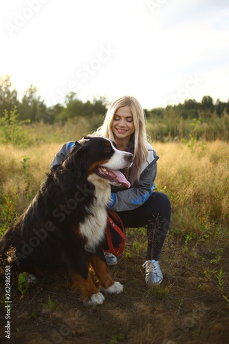 Young woman walking with Bernese Mountain Dog on the summer field