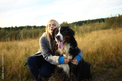 Young woman walking with Bernese Mountain Dog on the summer field