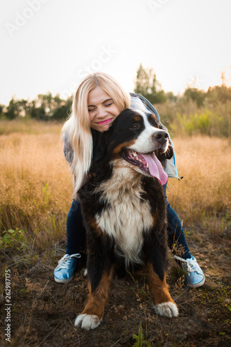 Young woman walking with Bernese Mountain Dog on the summer field