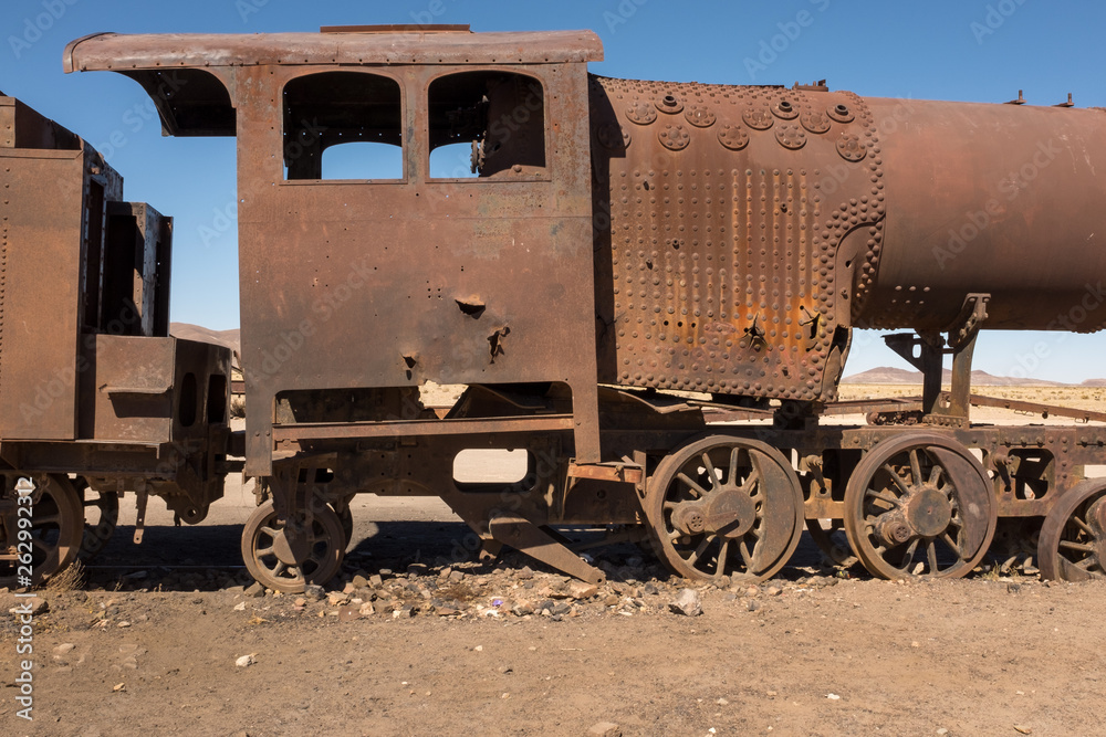 Side view of a rusting steam train as it slowly rots away at the train graveyard just outside of Uyuni, Bolivia, against a bright blue sky.