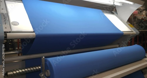 The garment factory takes a sample of a roll of blue fabric checking the quality of the roll checking on the machine the roll of fabric is unwound fully. Concept of: Checking quality, New fabric.