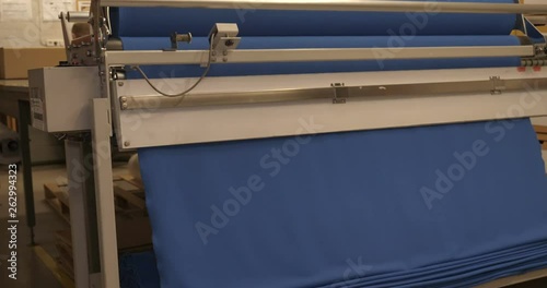 The garment factory takes a sample of a roll of blue fabric checking the quality of the roll checking on the machine the roll of fabric is unwound fully. Concept of: Checking quality, New fabric.