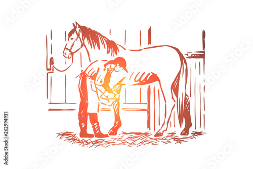 Young woman checking stallion horseshoe, equine care, female farmer in apron, purebred mare in stable