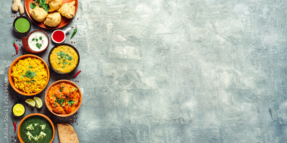 Indian cuisine dishes: tikka masala, dal, paneer, samosa, chapati, chutney, spices. Indian food on gray background. Assortment indian meal banner with copy space for text. Top view or flat lay. Indian cuisine dishes: tikka masala, dal, paneer, samosa, chapati, chutney, spices. Indian food on gray background. Assortment indian meal banner with copy space for text. Top view or flat lay.