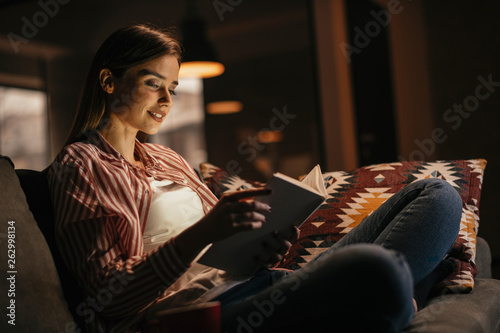 Girl at home studying. Teen reading a book on the couch.