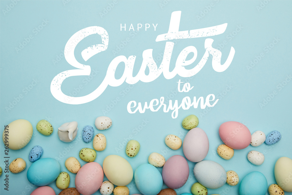 top view of painted multicolored eggs scattered near decorative bunny on blue background with happy Easter to everyone lettering top view of painted multicolored eggs scattered near decorative bunny on blue background with happy Easter to everyone lettering