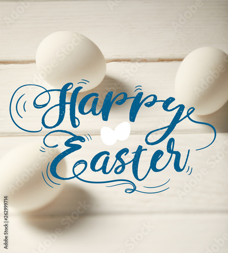 chicken eggs on white wooden table with blue happy Easter lettering © LIGHTFIELD STUDIOS