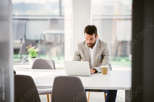 Businessman sitting looking at his laptop. Businessman working in the office on his laptop. Stylish businessman working on a project in the office thinking about future