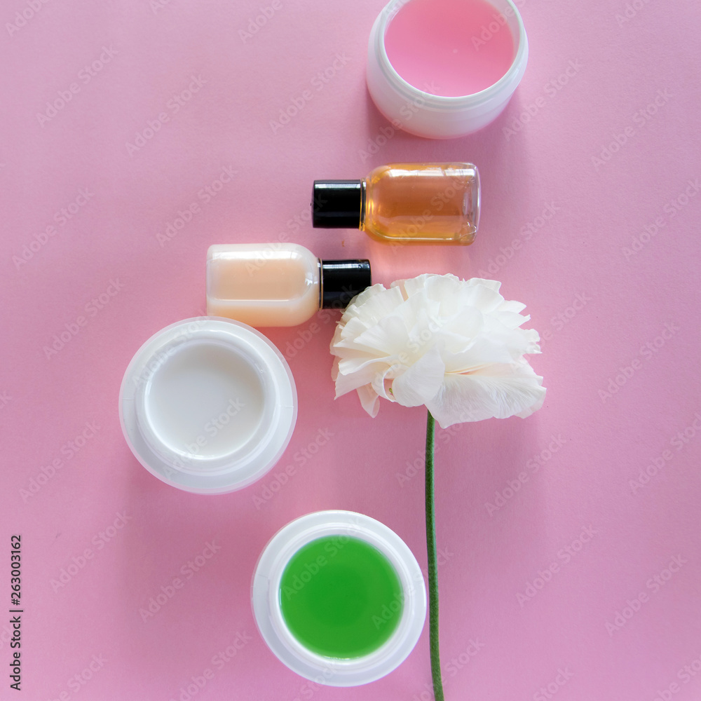 Top view of cosmetic products and delicate flowers on pink background. Wellness beauty treatment. Organic skin care products. Top view of cosmetic products and delicate flowers on pink background. Wellness beauty treatment. Organic skin care products.