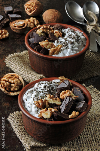 Two cups with yogurt with chia seeds, walnuts and dark chocolate. Breakfast or dessert for two. Healthy food. Keto diet. Diet recipes ideas. Shabby style. Dark background.